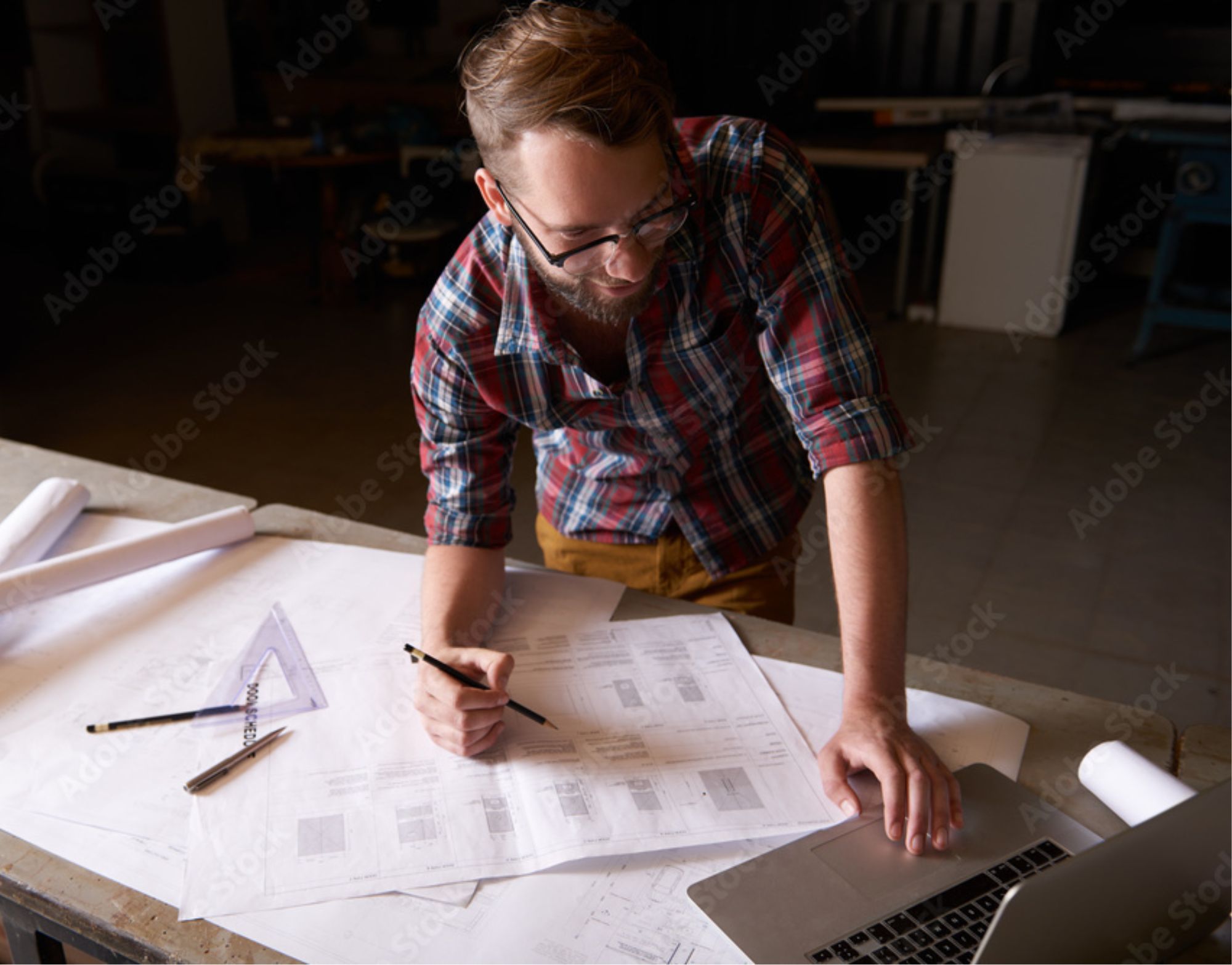 Contractor reviewing project plans and paperwork at a worktable with a laptop nearby